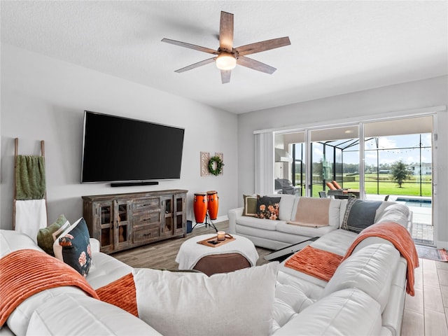 living room featuring light wood-style floors, a sunroom, ceiling fan, a textured ceiling, and baseboards