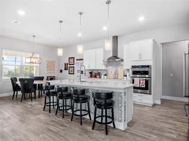 kitchen with light countertops, wall chimney range hood, and a center island with sink