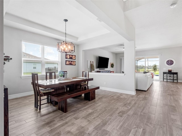 dining area with light wood-style floors, baseboards, a tray ceiling, and ceiling fan with notable chandelier