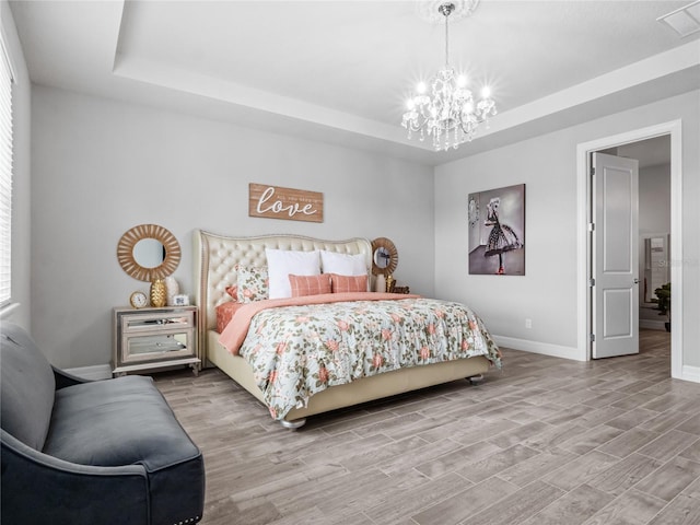 bedroom with a tray ceiling, wood finished floors, and visible vents