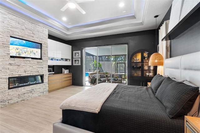 bedroom with a stone fireplace, crown molding, access to outside, a tray ceiling, and light hardwood / wood-style floors