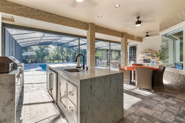 view of patio featuring area for grilling, exterior kitchen, an outdoor wet bar, ceiling fan, and glass enclosure