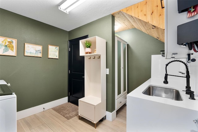 kitchen featuring washer / dryer, sink, light hardwood / wood-style flooring, and a textured ceiling