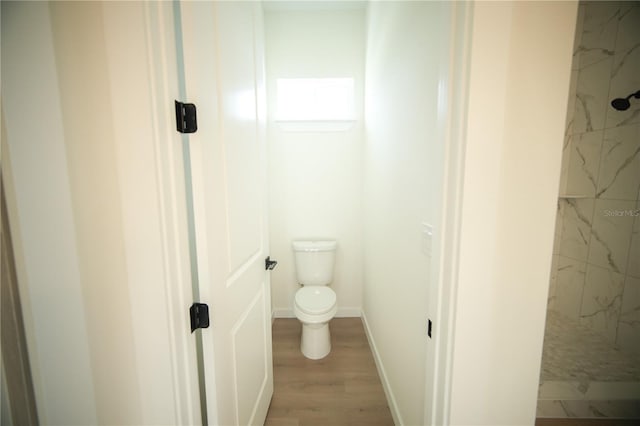 bathroom featuring a tile shower, hardwood / wood-style floors, and toilet