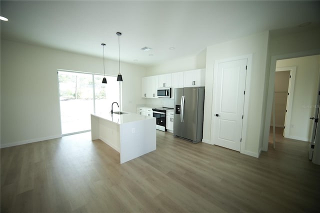 kitchen featuring sink, appliances with stainless steel finishes, white cabinetry, hanging light fixtures, and an island with sink