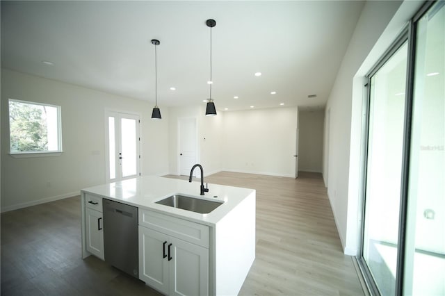 kitchen featuring sink, dishwasher, white cabinets, a center island with sink, and decorative light fixtures