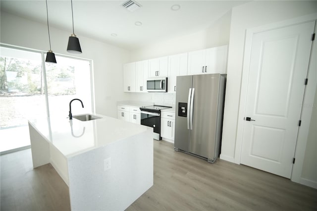 kitchen with sink, hanging light fixtures, appliances with stainless steel finishes, a kitchen island with sink, and white cabinets