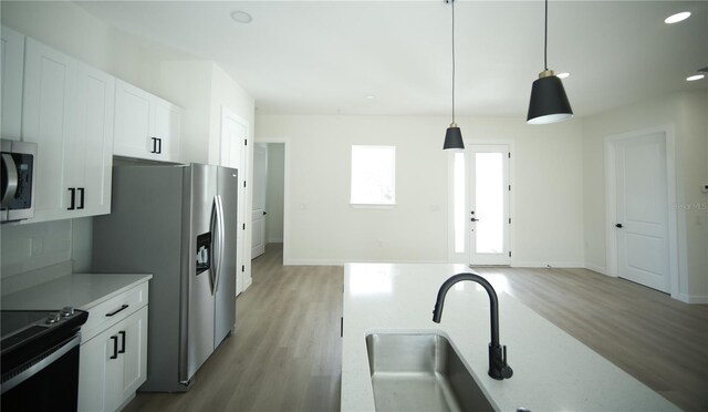 kitchen with appliances with stainless steel finishes, white cabinets, light wood-type flooring, and decorative light fixtures