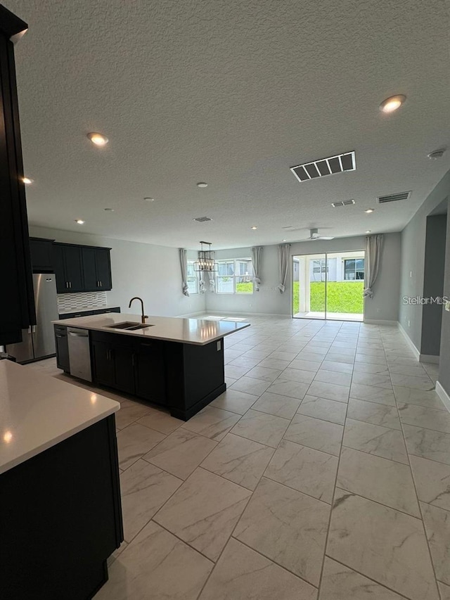 kitchen featuring stainless steel appliances, sink, a center island with sink, and a textured ceiling