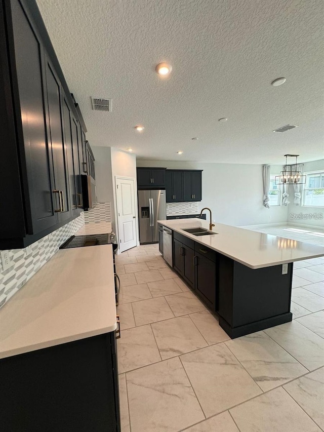 kitchen featuring appliances with stainless steel finishes, decorative light fixtures, sink, decorative backsplash, and a center island with sink