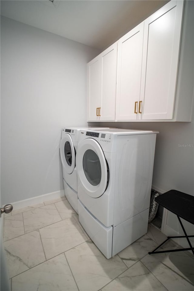 washroom featuring marble finish floor, washer and clothes dryer, cabinet space, and baseboards