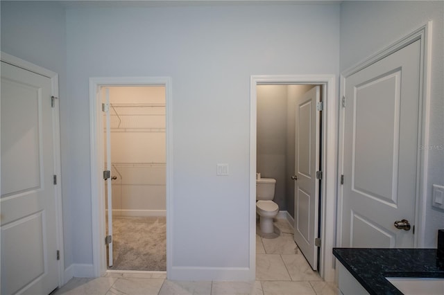 bathroom featuring a walk in closet, baseboards, vanity, and toilet