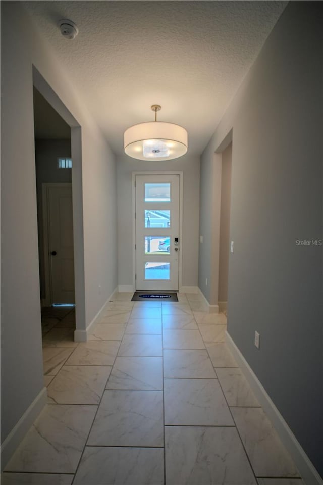 doorway with marble finish floor, a textured ceiling, and baseboards