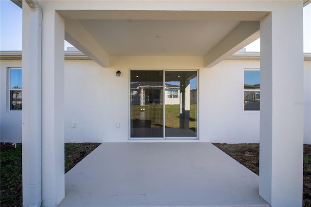 view of exterior entry with a patio and stucco siding