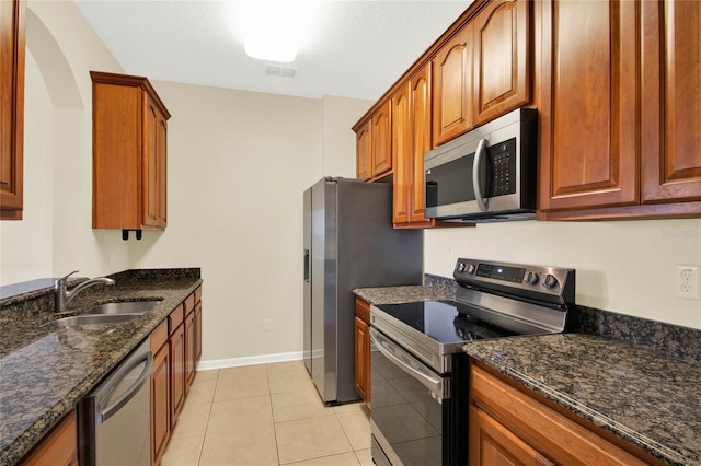 kitchen with stainless steel appliances, sink, dark stone countertops, and light tile patterned floors