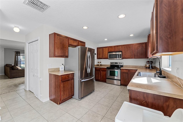 kitchen with appliances with stainless steel finishes, sink, a textured ceiling, and light tile patterned floors