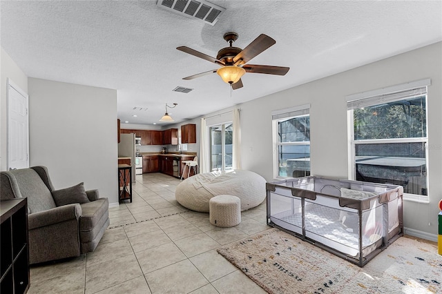 living room featuring light tile patterned flooring, ceiling fan, sink, and a textured ceiling