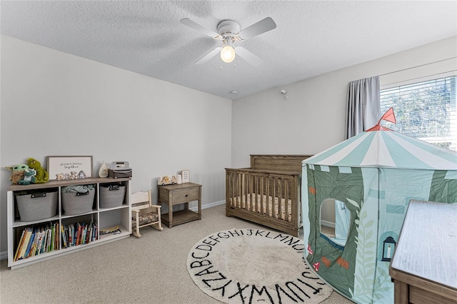 bedroom with ceiling fan, a nursery area, a textured ceiling, and carpet flooring