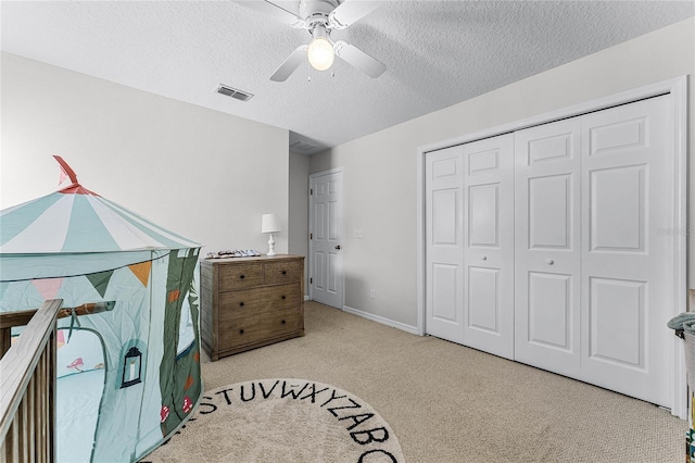 bedroom featuring ceiling fan, light colored carpet, a closet, and a textured ceiling