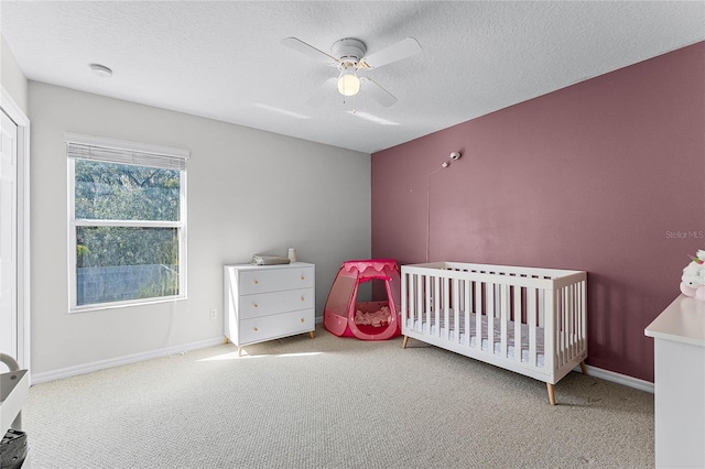 carpeted bedroom featuring a textured ceiling, a crib, and ceiling fan