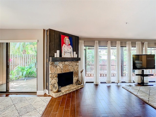 unfurnished living room with hardwood / wood-style flooring, a stone fireplace, and a wealth of natural light