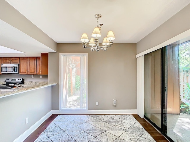 kitchen featuring dark wood-type flooring, appliances with stainless steel finishes, an inviting chandelier, light stone counters, and decorative light fixtures