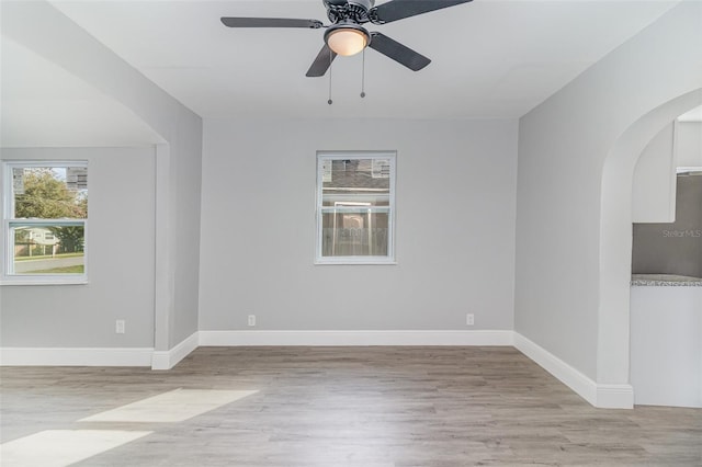 empty room with a healthy amount of sunlight, ceiling fan, and light hardwood / wood-style flooring