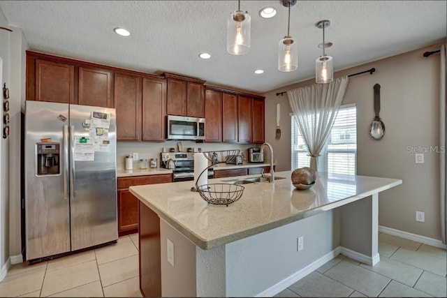 kitchen featuring sink, appliances with stainless steel finishes, a kitchen island with sink, light stone counters, and decorative light fixtures