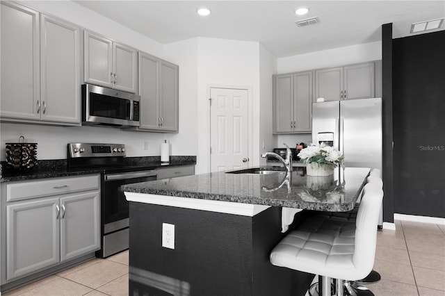 kitchen with sink, light tile patterned floors, appliances with stainless steel finishes, gray cabinetry, and an island with sink