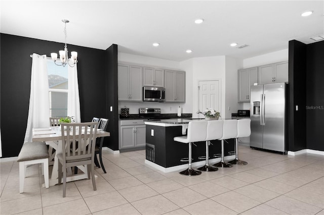 kitchen featuring appliances with stainless steel finishes, gray cabinetry, a center island with sink, and pendant lighting