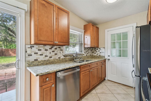 kitchen featuring light tile patterned floors, decorative backsplash, brown cabinets, appliances with stainless steel finishes, and a sink