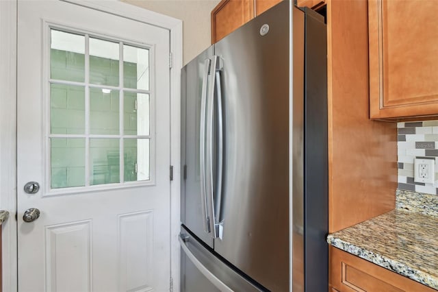 kitchen with brown cabinets, backsplash, light stone countertops, and freestanding refrigerator