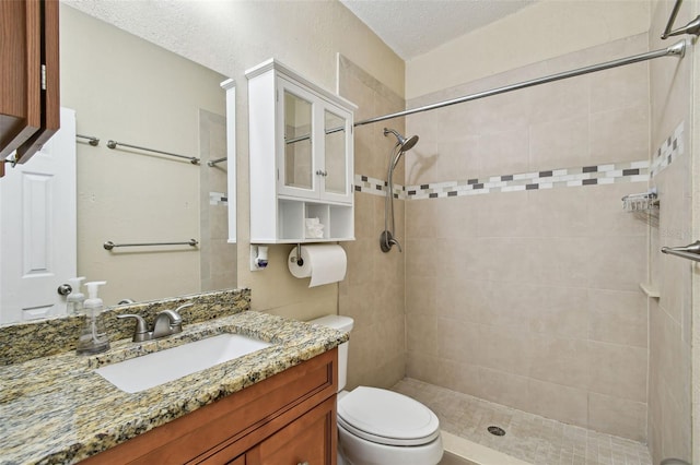 bathroom with tiled shower, vanity, toilet, and a textured ceiling