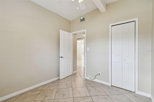 unfurnished bedroom featuring light tile patterned floors, lofted ceiling with beams, a closet, and ceiling fan