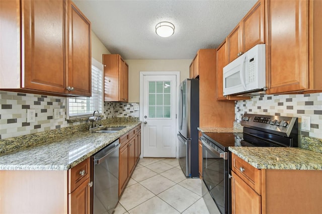 kitchen with brown cabinets, a sink, tasteful backsplash, stainless steel appliances, and light tile patterned floors