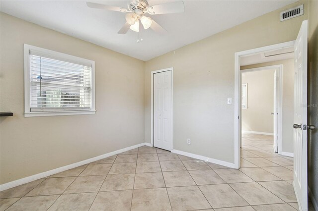 unfurnished bedroom with visible vents, a closet, light tile patterned floors, baseboards, and ceiling fan