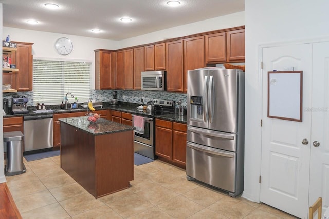 kitchen featuring light tile patterned flooring, appliances with stainless steel finishes, tasteful backsplash, dark stone counters, and a center island