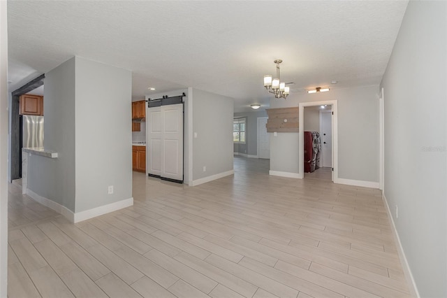 unfurnished room featuring a notable chandelier, a barn door, washing machine and dryer, and light wood-type flooring