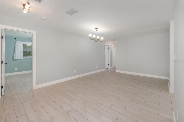 unfurnished room featuring a chandelier, a textured ceiling, and light hardwood / wood-style floors