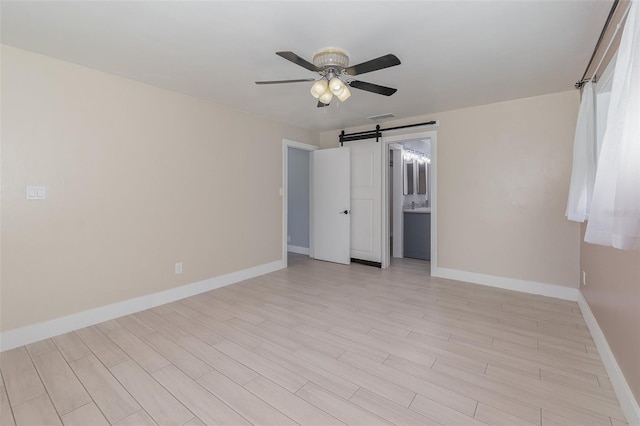 unfurnished room with a barn door, light wood-type flooring, and ceiling fan