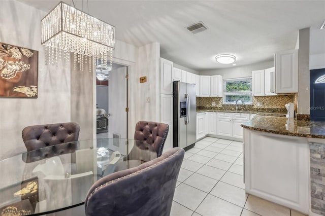 kitchen with pendant lighting, stainless steel fridge, dark stone countertops, backsplash, and white cabinets