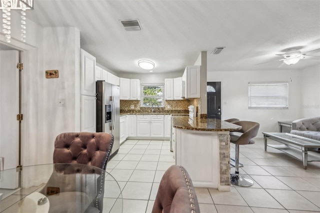 kitchen featuring stainless steel fridge with ice dispenser, light tile patterned floors, a breakfast bar, and white cabinets