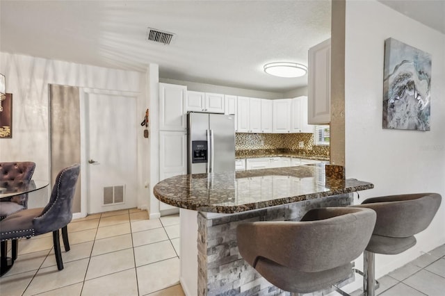 kitchen with white cabinetry, a breakfast bar area, stainless steel fridge, and kitchen peninsula