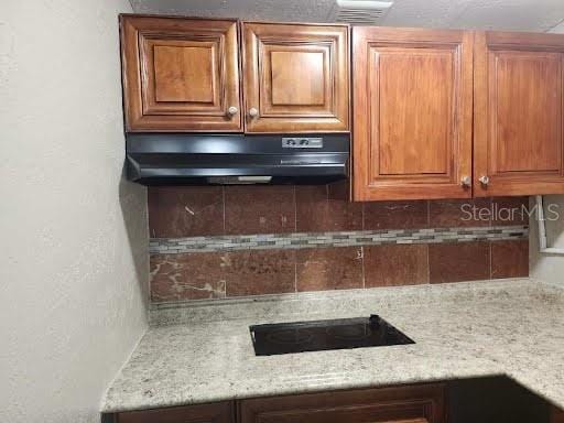 kitchen with tasteful backsplash, light stone countertops, and black electric stovetop