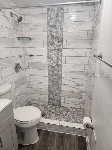 bathroom featuring hardwood / wood-style flooring, vanity, tiled shower, and toilet