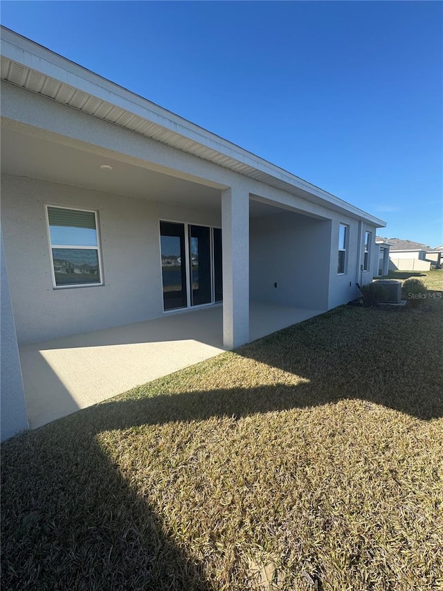 rear view of house featuring a patio, cooling unit, a yard, and stucco siding