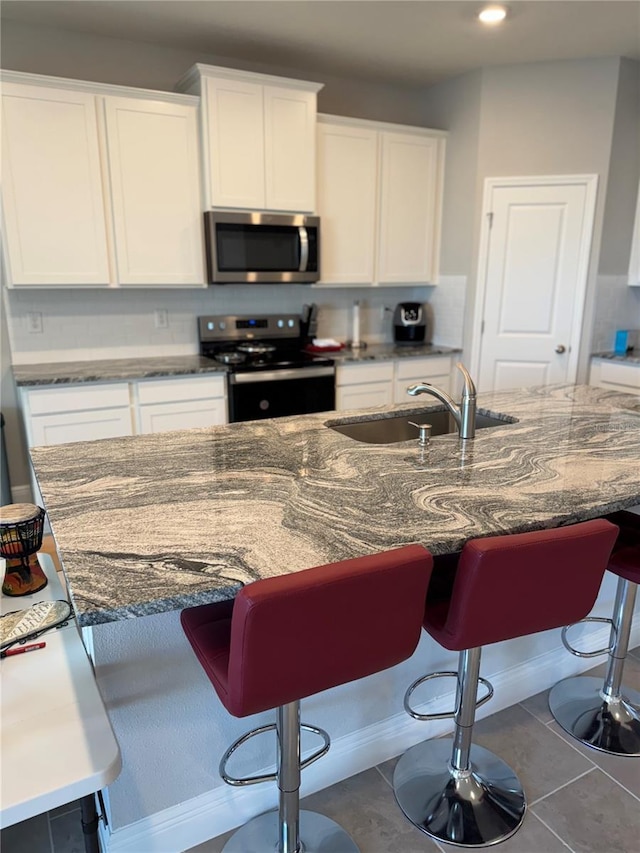 kitchen featuring dark stone counters, a sink, stainless steel appliances, white cabinetry, and tile patterned floors