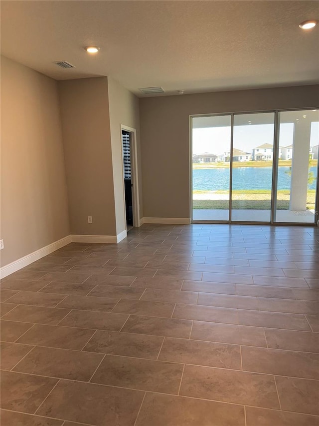 spare room with visible vents, baseboards, a water view, recessed lighting, and a textured ceiling