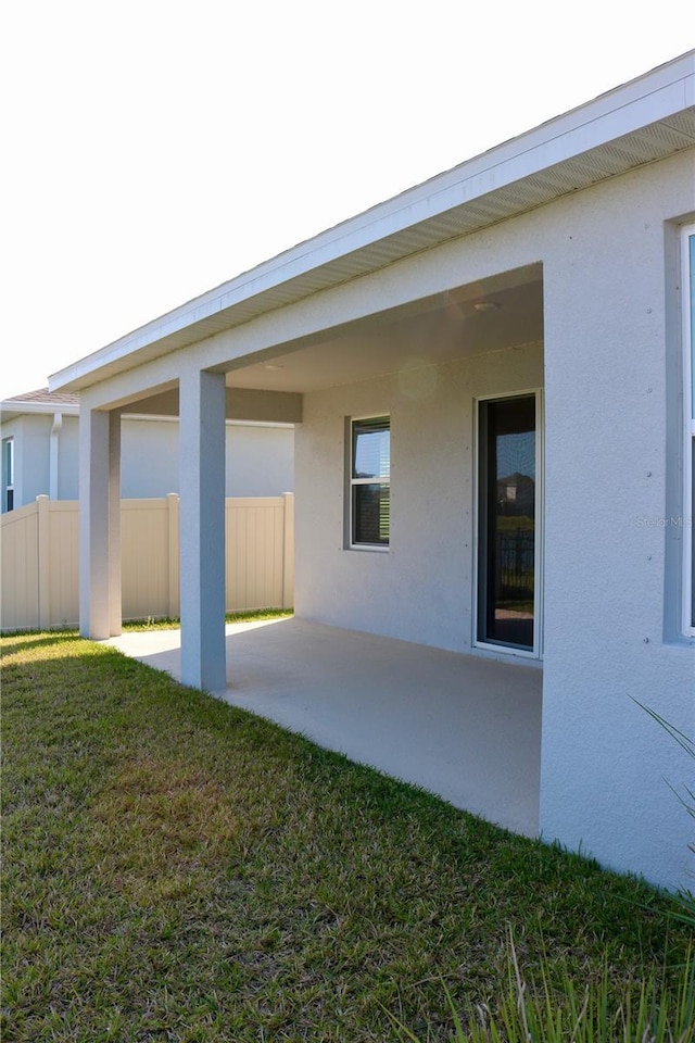 back of house featuring stucco siding, a lawn, and fence