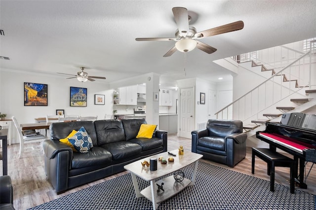 living room featuring a textured ceiling, wood-type flooring, ornamental molding, and ceiling fan